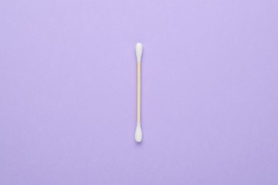 Photo of One wooden cotton bud on violet background, top view