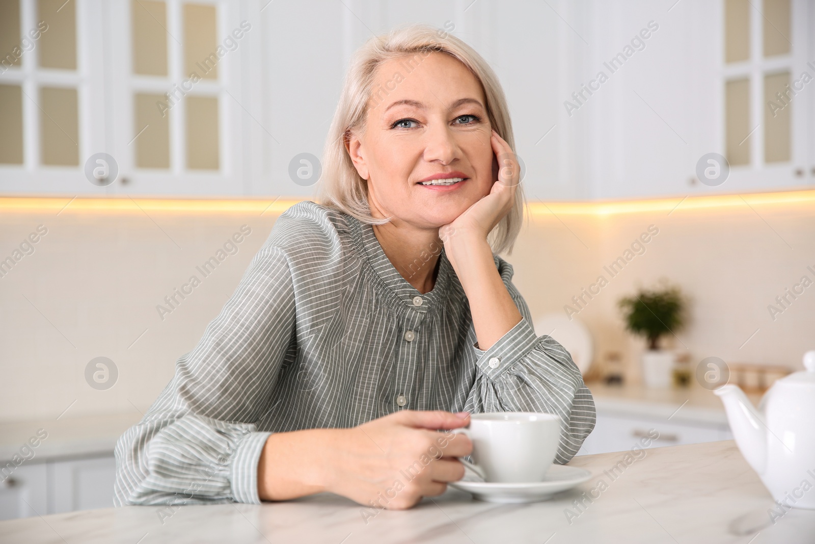 Photo of Beautiful mature woman with cup of coffee in kitchen