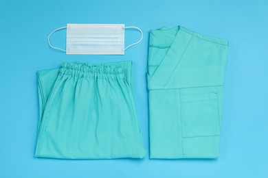 Photo of Medical uniform and protective mask on light blue background, flat lay