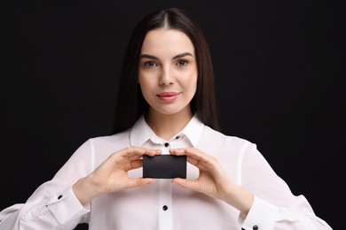 Woman holding blank business card on black background