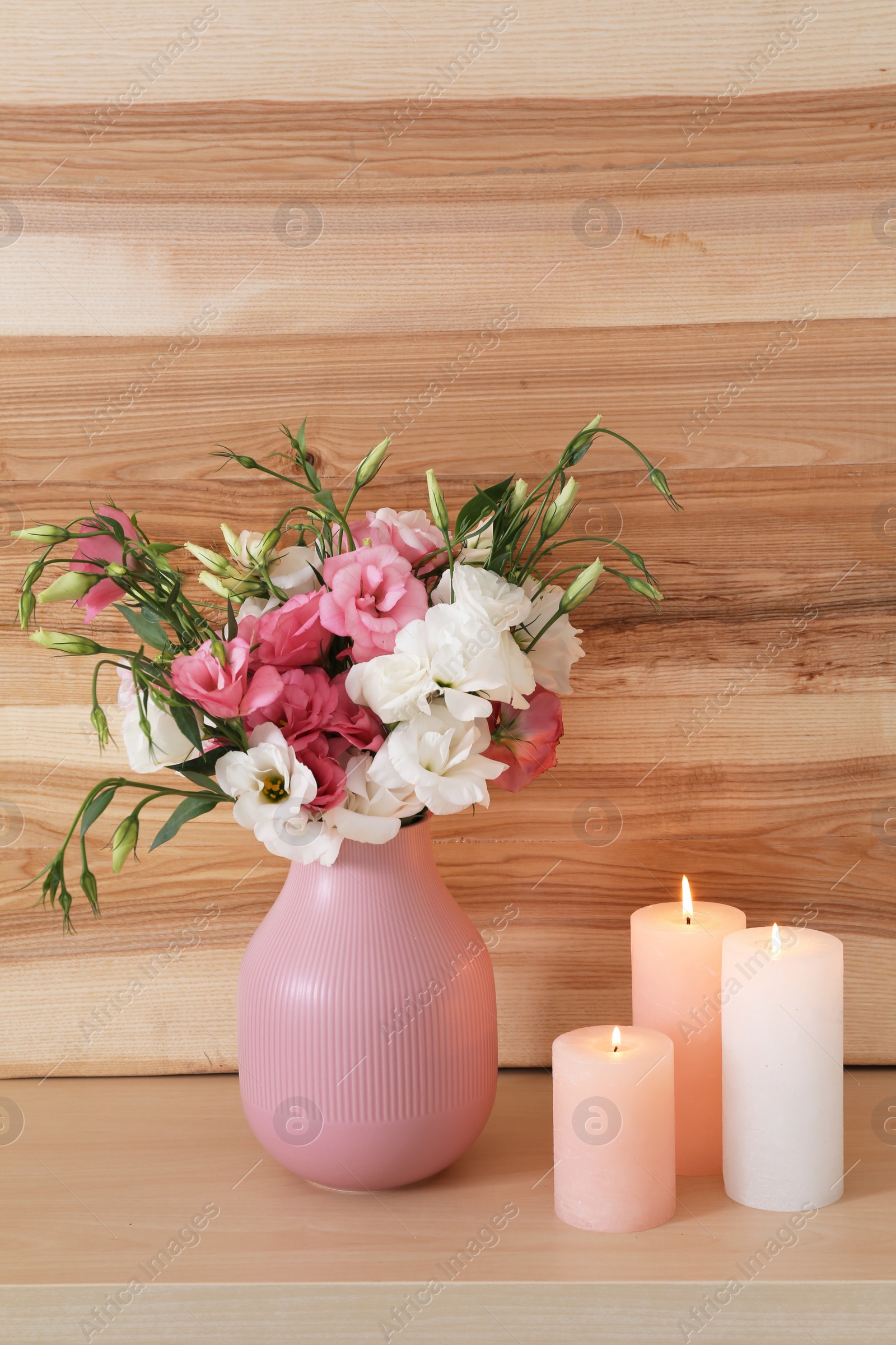 Photo of Burning candles and vase with flowers on table against wooden wall