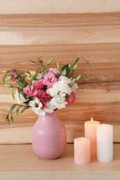 Burning candles and vase with flowers on table against wooden wall