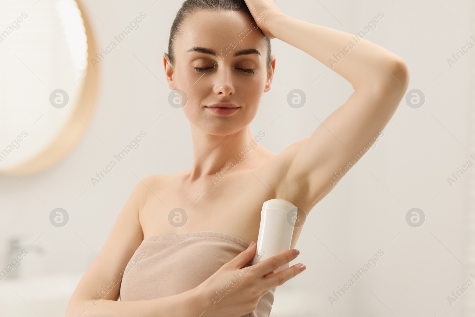 Photo of Beautiful young woman applying deodorant in bathroom