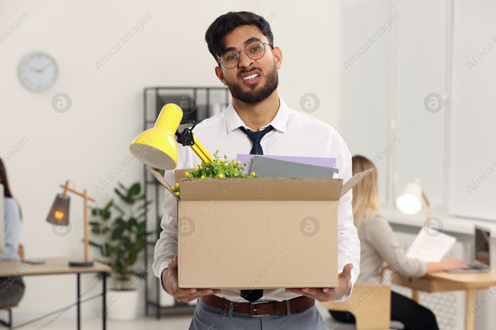 Photo of Unemployment problem. Frustrated man with box of personal belongings in office