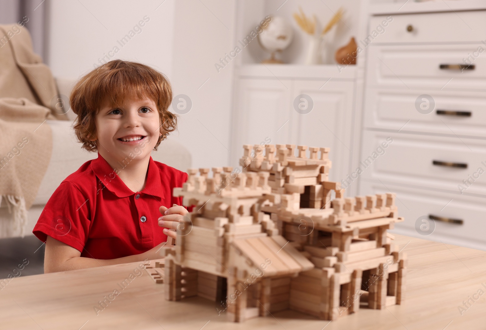 Photo of Cute little boy playing with wooden castle at table in room. Child's toy