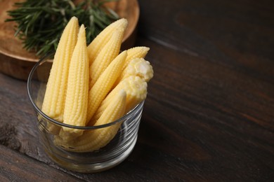 Photo of Tasty fresh yellow baby corns in glass on wooden table, space for text