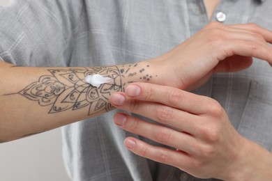 Photo of Tattooed woman applying cream onto her hand on light background, closeup