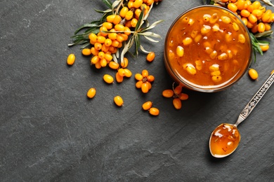 Photo of Delicious sea buckthorn jam and fresh berries on black table, flat lay. Space for text