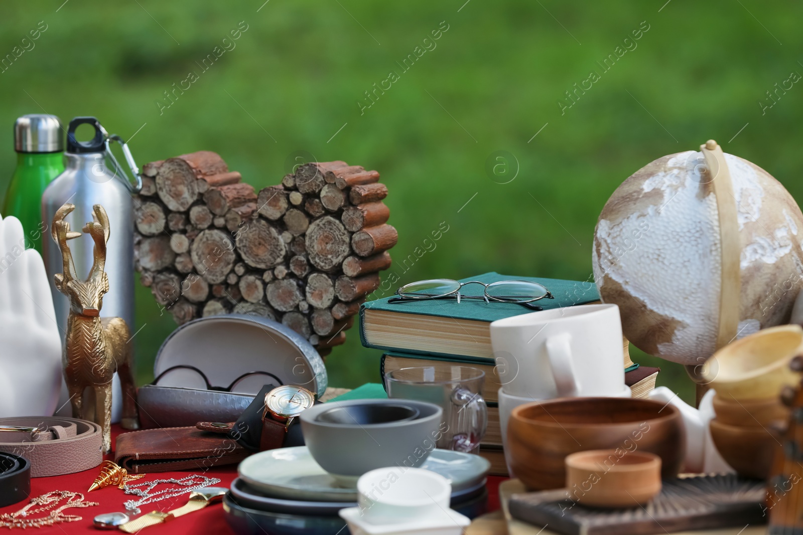 Photo of Many different items on red tablecloth outdoors. Garage sale