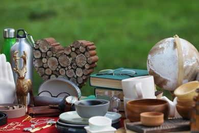 Many different items on red tablecloth outdoors. Garage sale