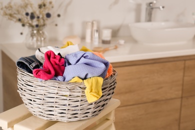 Photo of Wicker laundry basket with different clothes on wooden stool in bathroom. Space for text