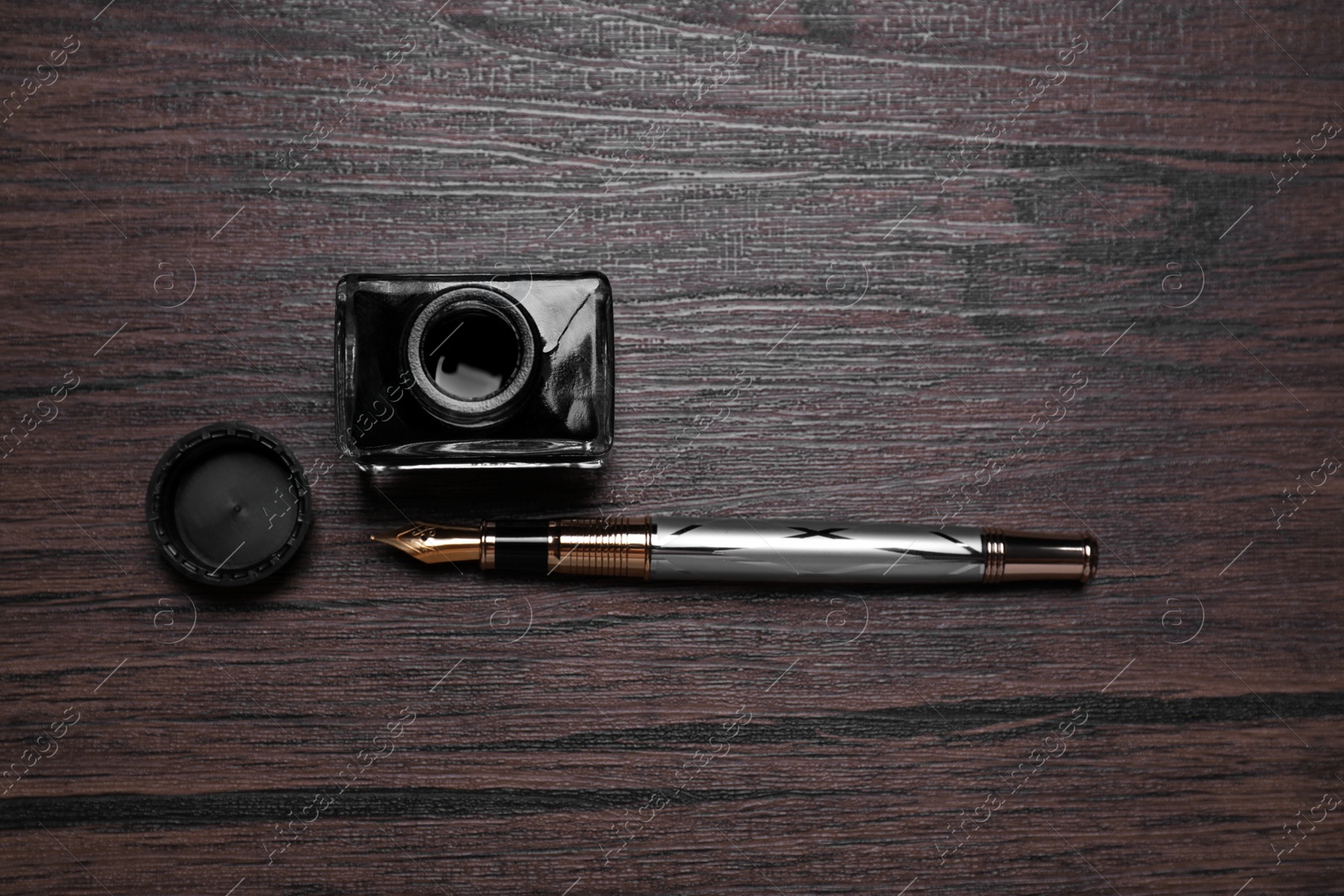 Photo of Inkwell and fountain pen on wooden table, flat lay