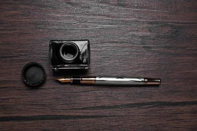 Photo of Inkwell and fountain pen on wooden table, flat lay