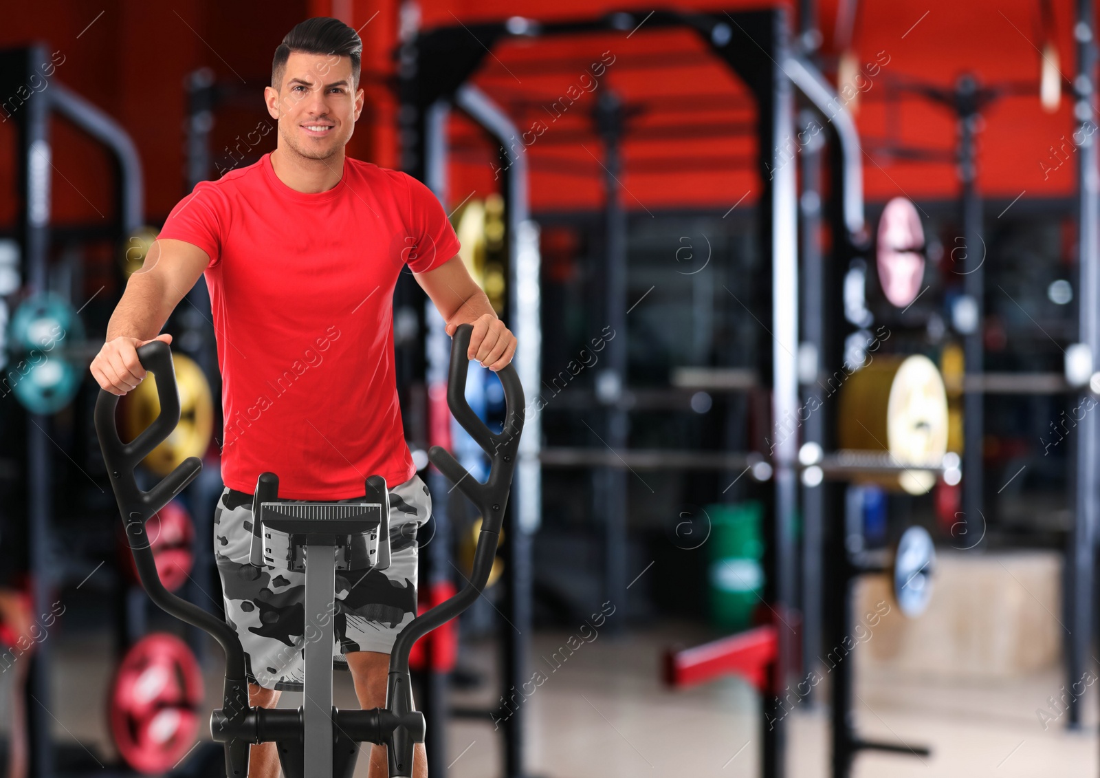 Image of Man using modern elliptical machine in gym, space for text