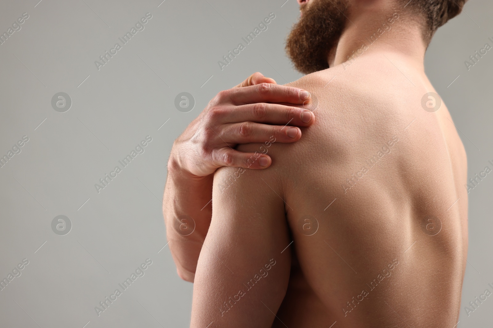 Photo of Man touching his shoulder on light grey background, closeup. Space for text