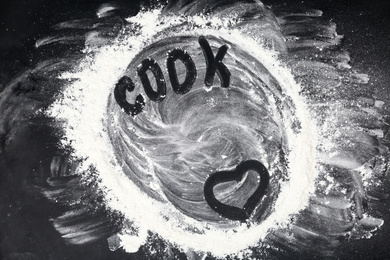 Heart and word COOK written on flour scattered over black table, top view