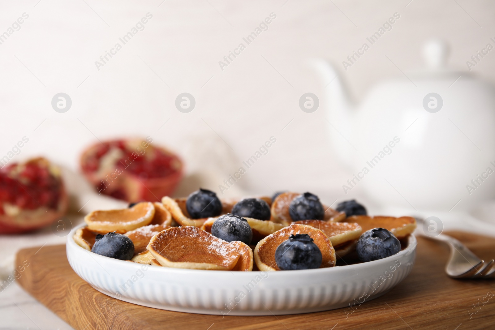 Photo of Delicious mini pancakes cereal with blueberries on wooden board