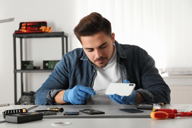 Photo of Technician repairing broken smartphone at table in workshop