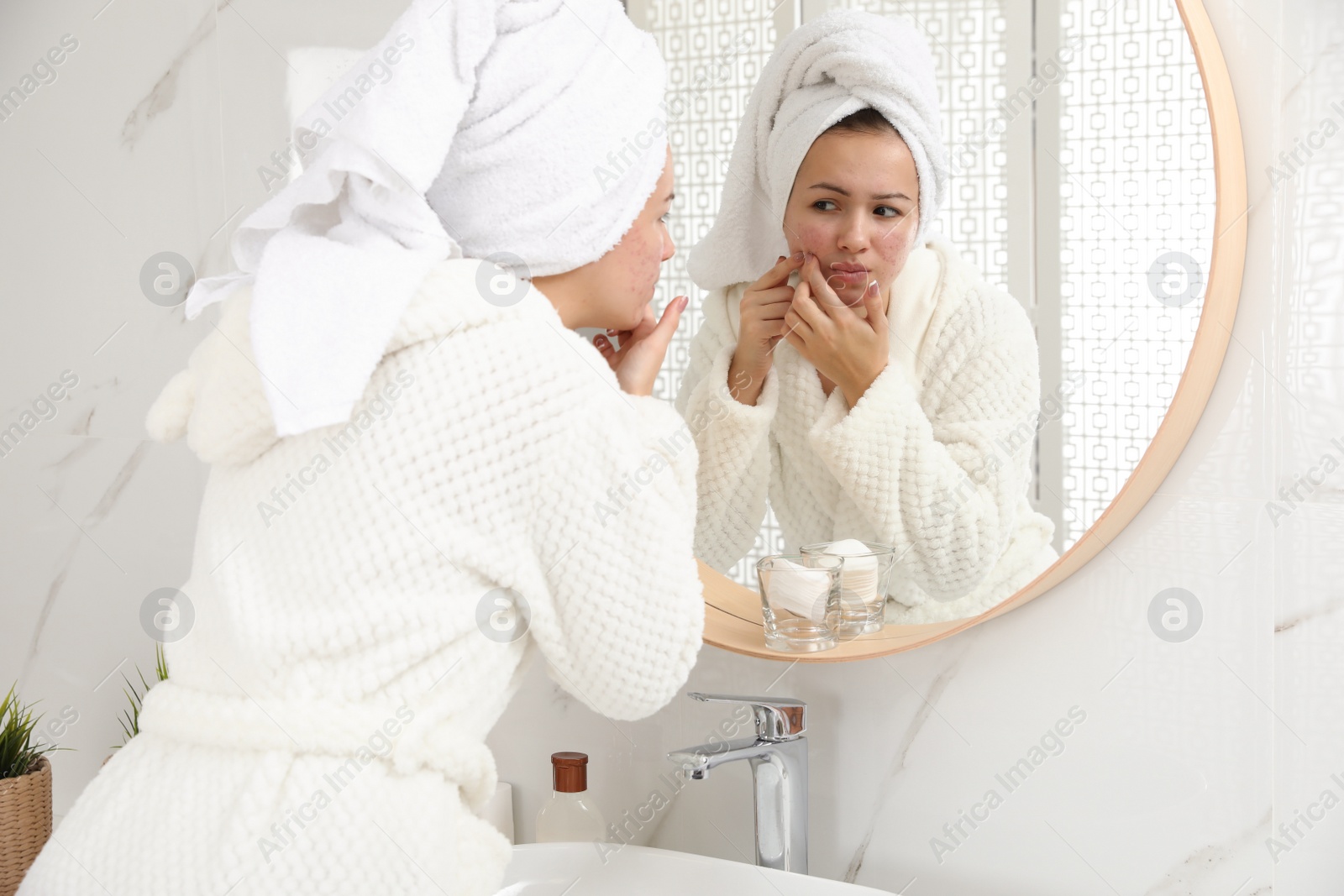 Photo of Teen girl with acne problem squeezing pimple near mirror in bathroom