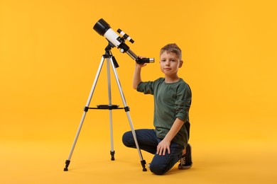 Cute little boy with telescope on orange background