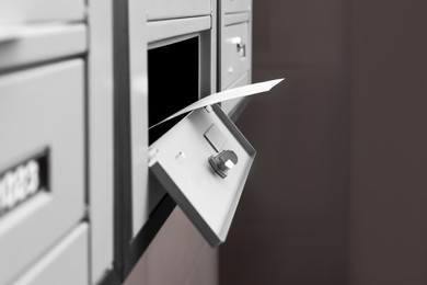 Photo of Open metal mailbox with envelope indoors, closeup view