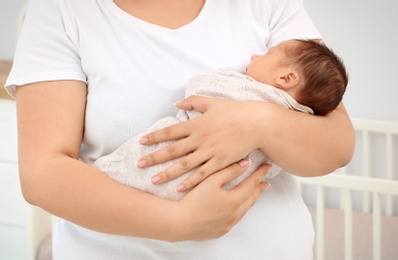 Young mother holding cute newborn baby at home