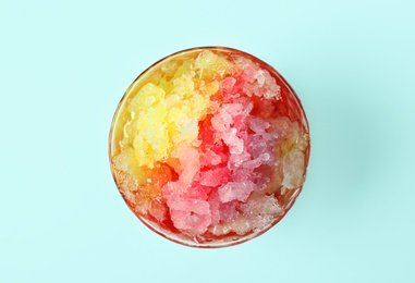 Rainbow shaving ice in glass dessert bowl on light blue background, top view