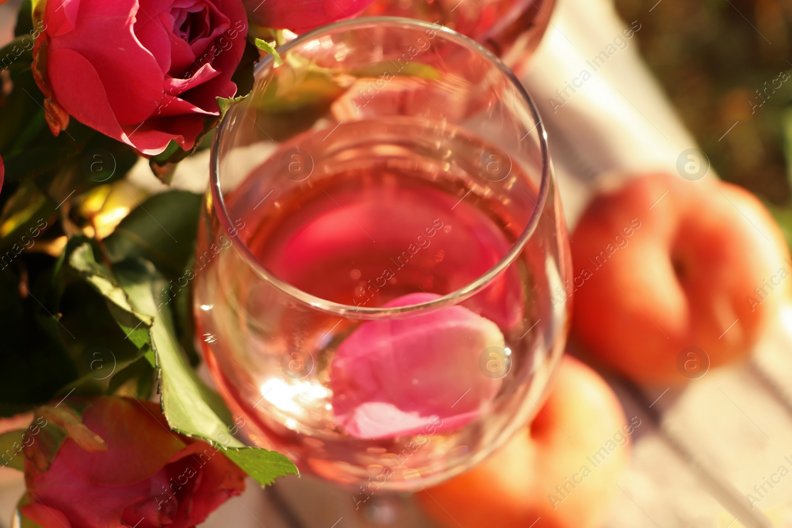 Photo of Glass of delicious rose wine with petals and flowers on outside, closeup