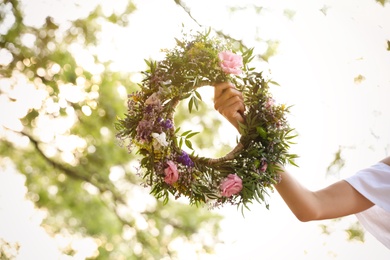 Photo of Young woman holding wreath made of beautiful flowers outdoors on sunny day, closeup