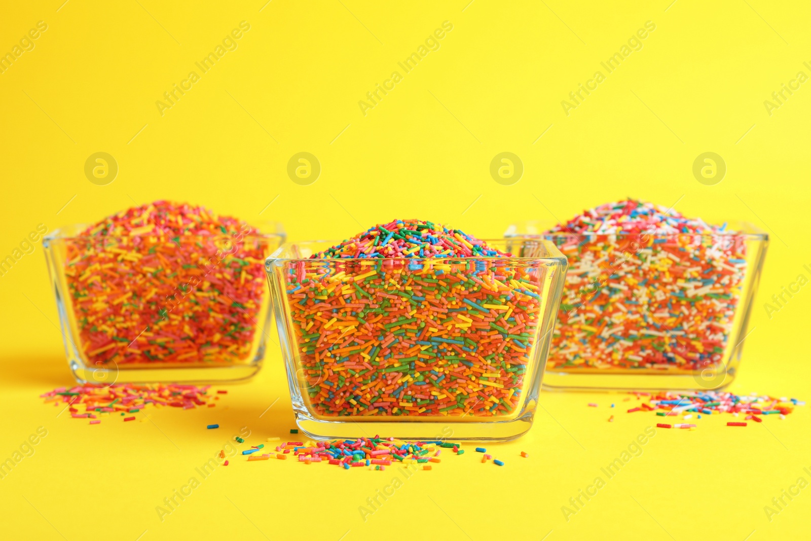 Photo of Colorful sprinkles in bowls on yellow background. Confectionery decor