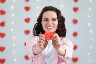 Photo of Beautiful young woman with red paper heart indoors, view from camera. Valentine's day celebration in long distance relationship