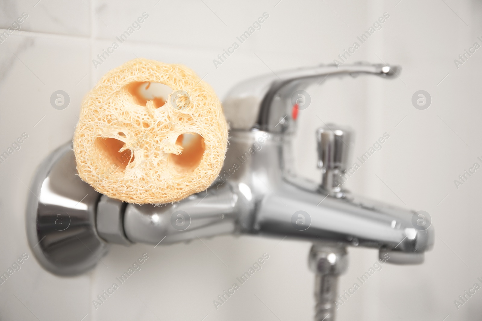 Photo of Natural loofah sponge on faucet in bathroom, closeup