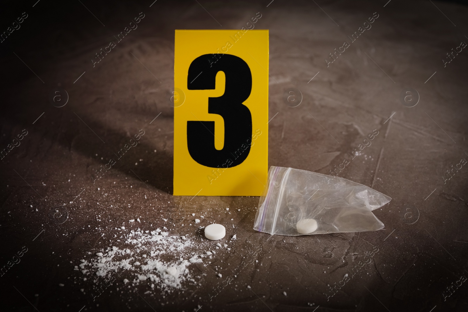 Photo of Pill and white powder near crime scene marker on grey stone table