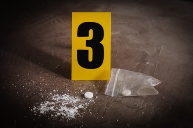 Pill and white powder near crime scene marker on grey stone table