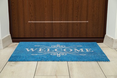 Photo of Beautiful blue doormat with word Welcome on floor near entrance