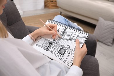 Image of Woman sketching kitchen interior in notebook with pencil at home, closeup