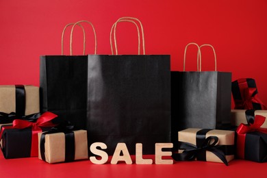 Photo of Word Sale made of wooden letters, shopping bags and gift boxes on red background. Black Friday