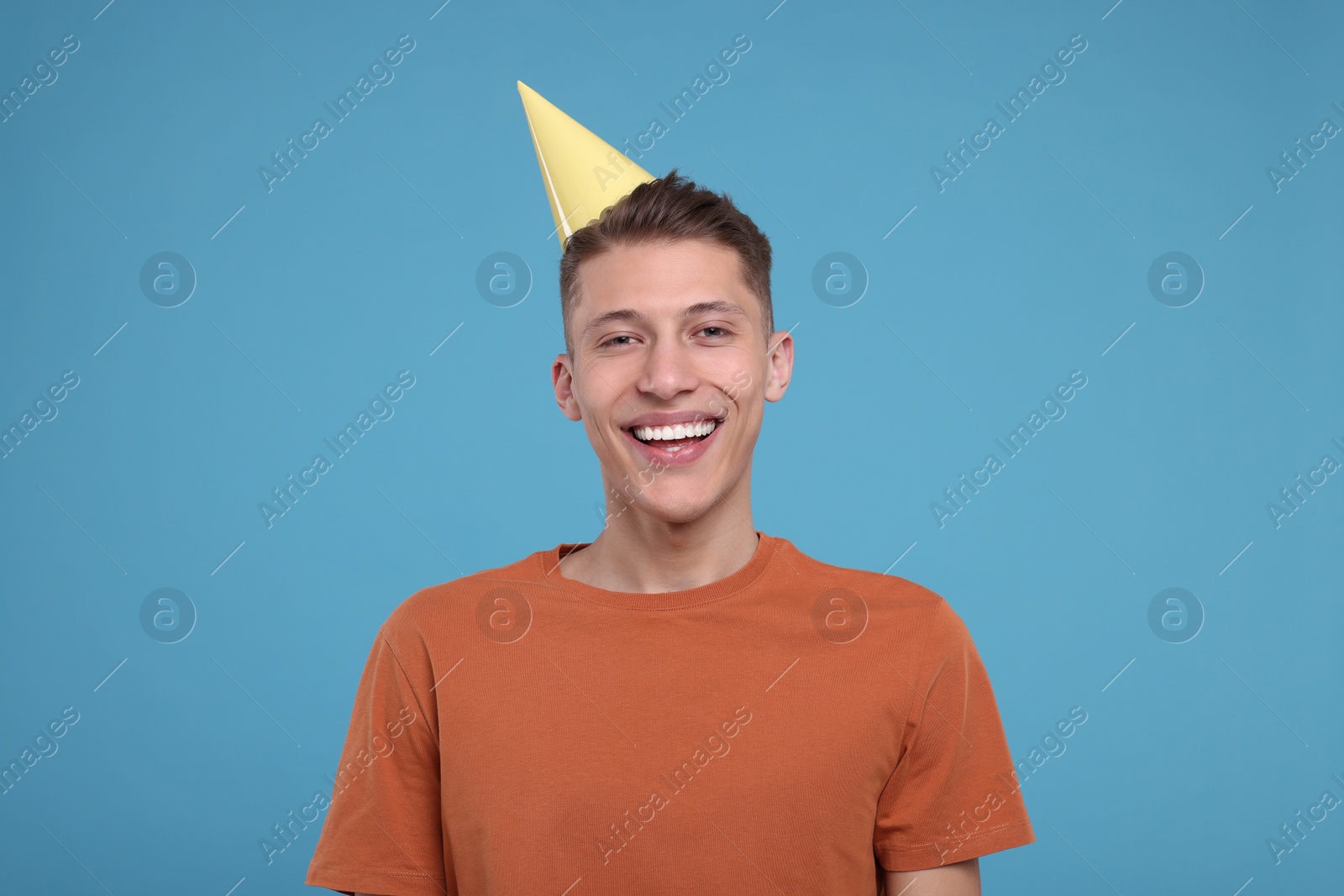 Photo of Happy young man in party hat on light blue background