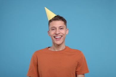 Happy young man in party hat on light blue background