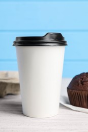 Photo of Paper cup with black lid on white wooden table. Coffee to go
