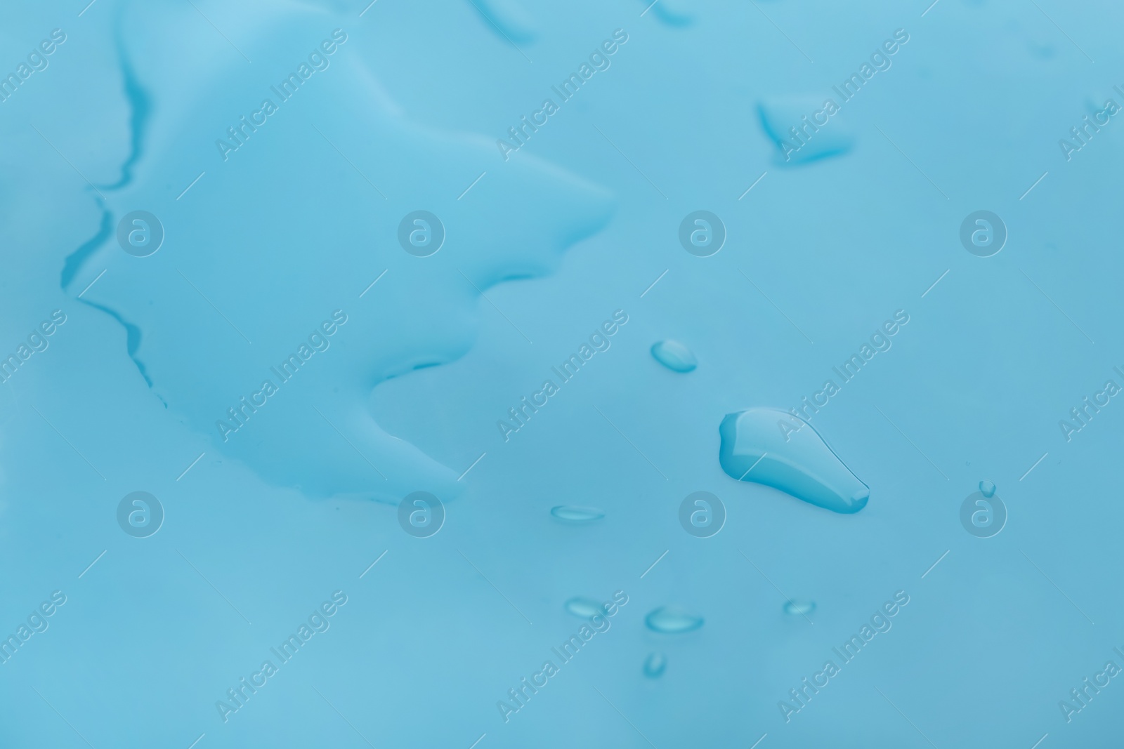 Photo of Drops of spilled water on light blue background, closeup