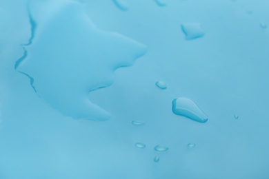 Photo of Drops of spilled water on light blue background, closeup