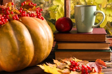 Photo of Stack of books, cup with aromatic tea, pumpkin and dry leaves on wooden windowsill indoors. Autumn atmosphere