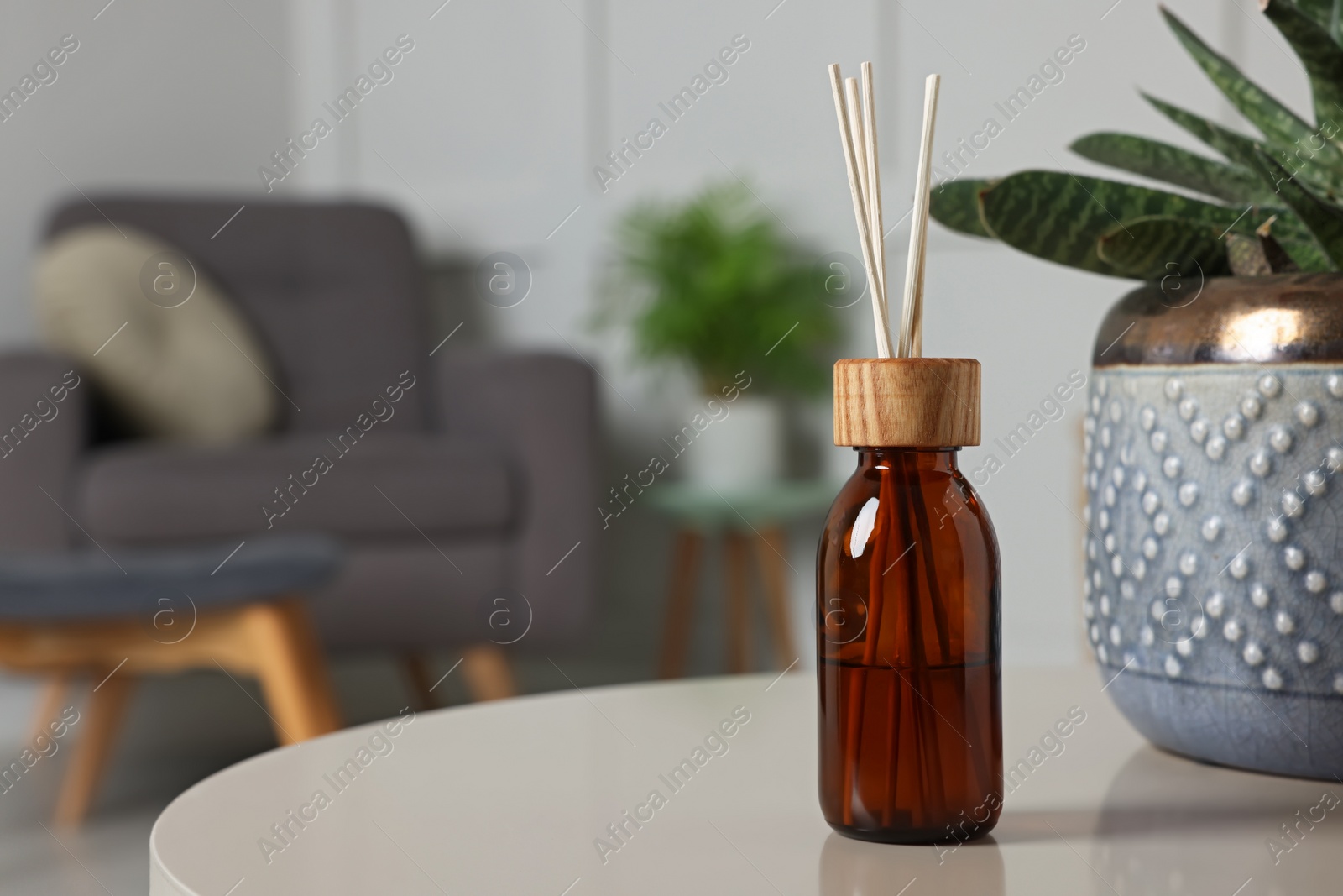 Photo of Aromatic reed air freshener near houseplant on light table indoors. Space for text