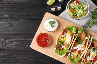 Photo of Delicious fish tacos served on dark wooden table, flat lay