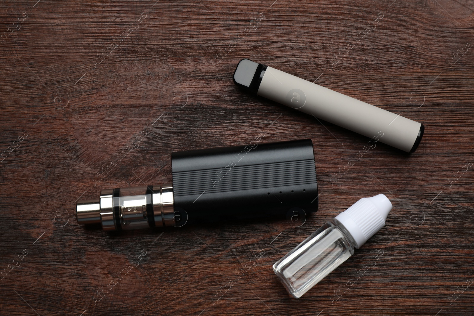 Photo of Different electronic cigarettes and vaping liquid on wooden table, flat lay. Smoking alternative