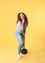 Curly African-American woman singing in microphone on color background