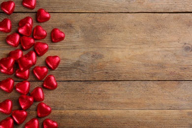 Photo of Heart shaped chocolate candies on wooden table, flat lay. Space for text