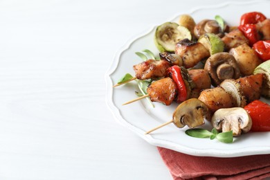 Photo of Delicious shish kebabs with vegetables and microgreens on white table, closeup. Space for text