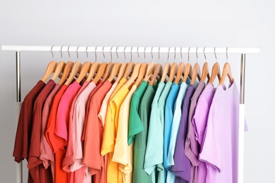 Photo of Rack with rainbow clothes on light background